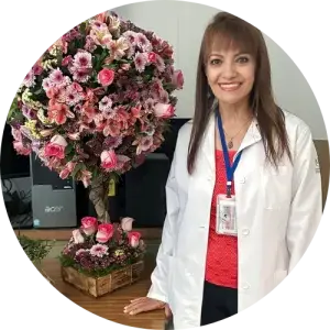Dr. Rosy Garcia, standing, wearing a white lab coat, next to a beautiful floral arrangement.